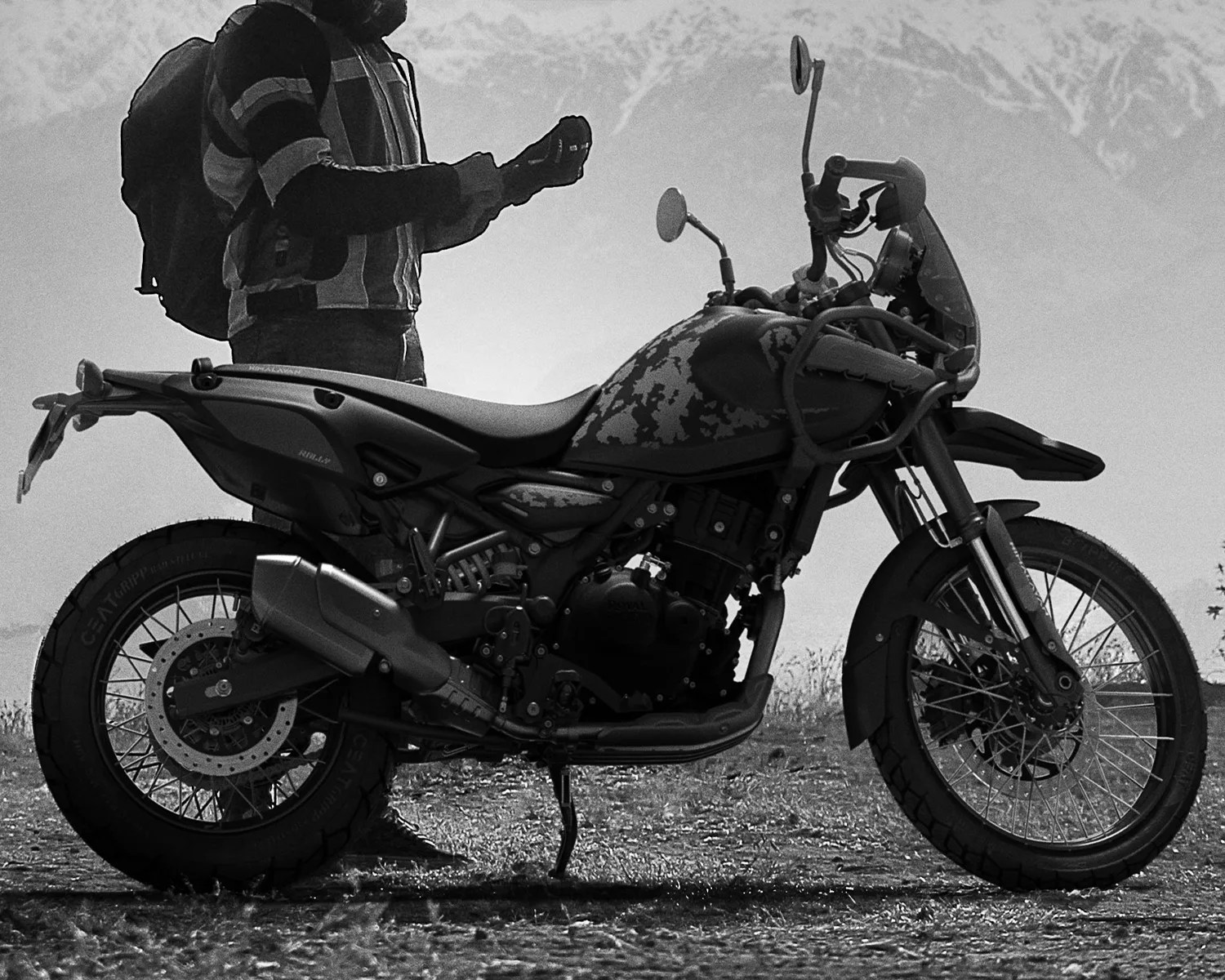 Black and gray adventure motorcycle with knobby tires parked on dirt with a person wearing a backpack standing behind it.