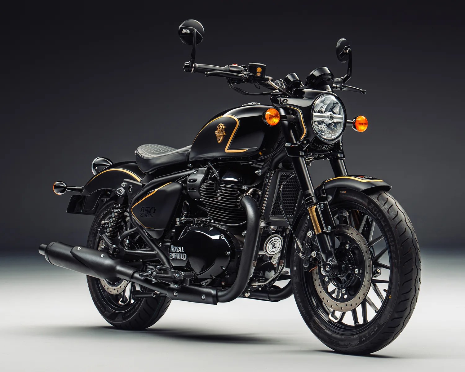 Black Royal Enfield 650 Shotgun motorcycle with gold trim and round headlight on a gray background.