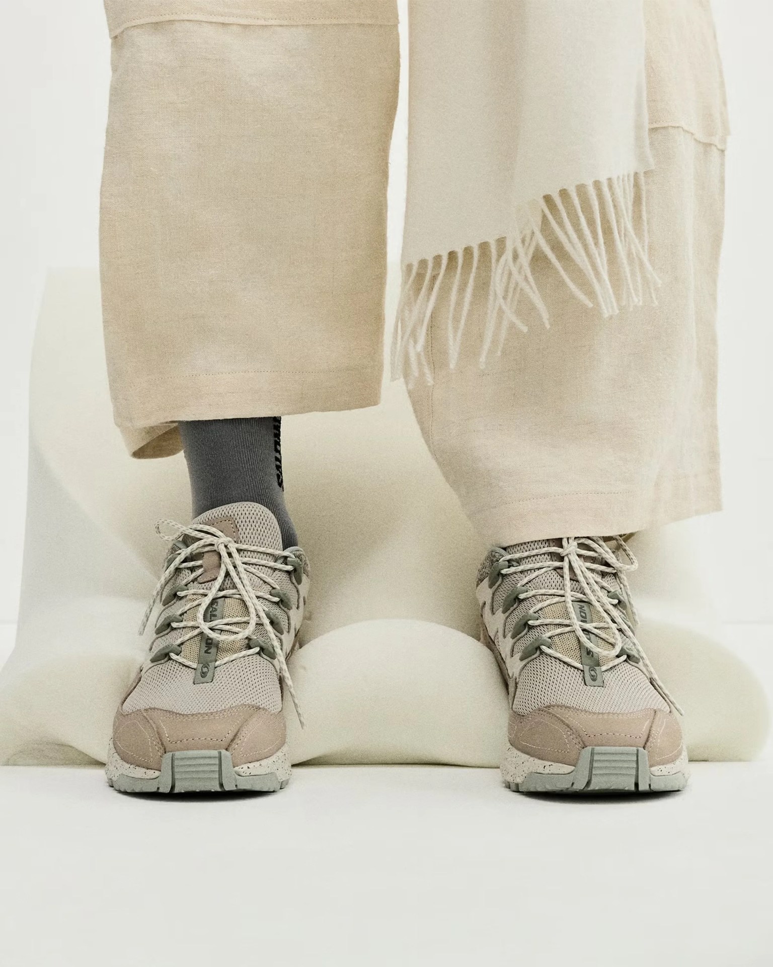 Pair of beige and gray mesh sneakers with laces worn with beige pants and gray socks.