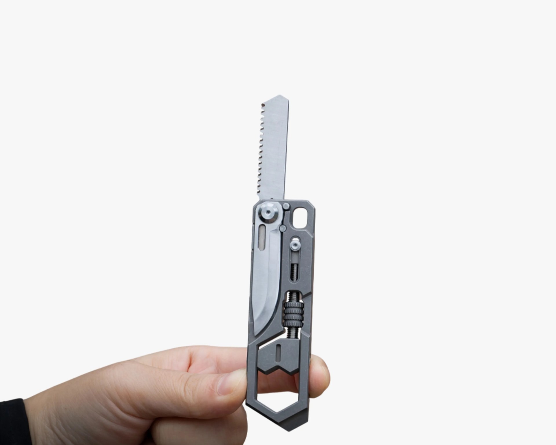 Hand holding a compact multi-tool with a partially serrated blade and various metal components.