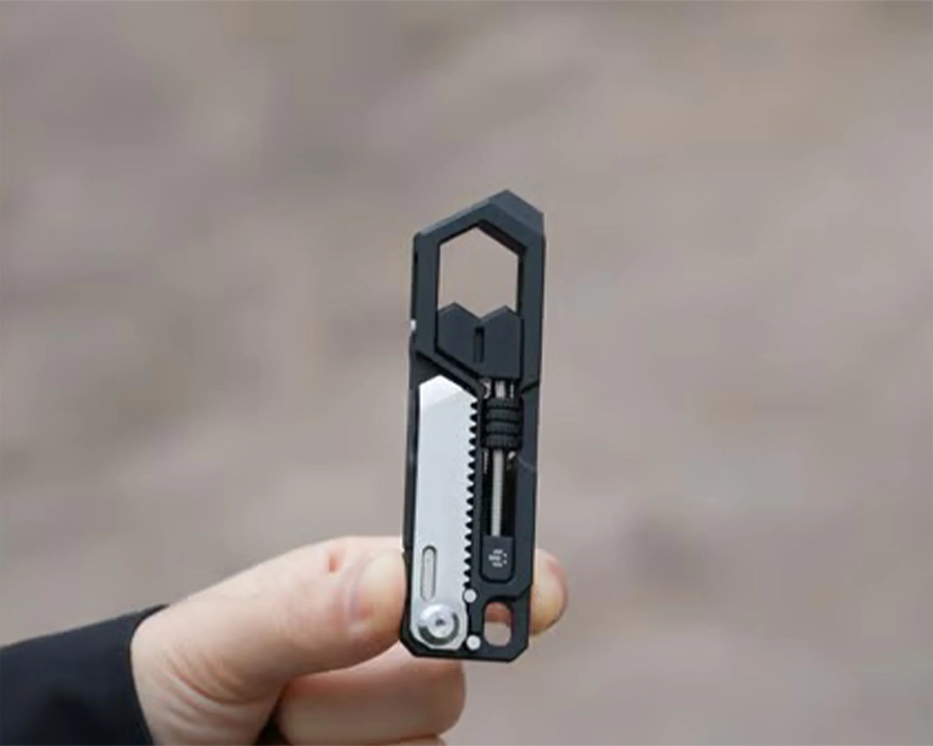 Compact black and silver multi-tool with a carabiner clip held in a hand.