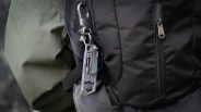Metal multi-tool with a carabiner clip attached to a black backpack strap.