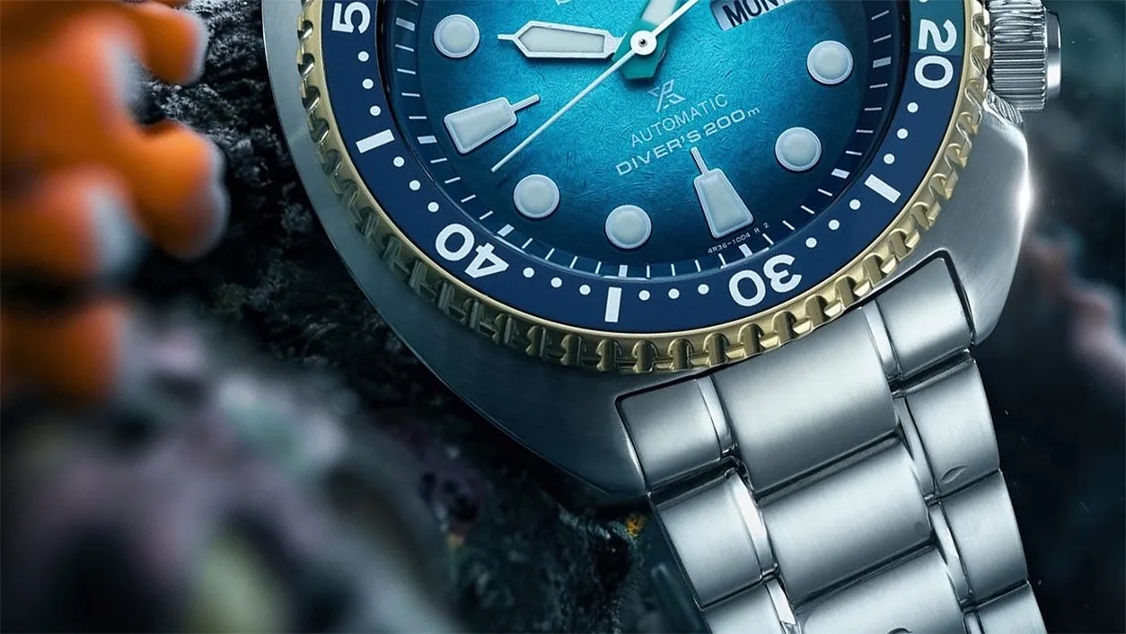 Close-up of a stainless steel diver's watch with a blue dial and gold-accented bezel on a dark textured surface.