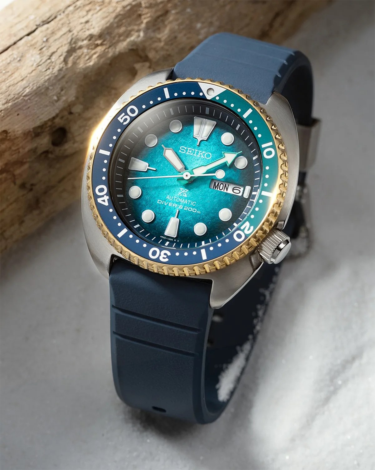 Seiko automatic diver's watch with blue-green dial, gold and blue bezel, and blue rubber strap.