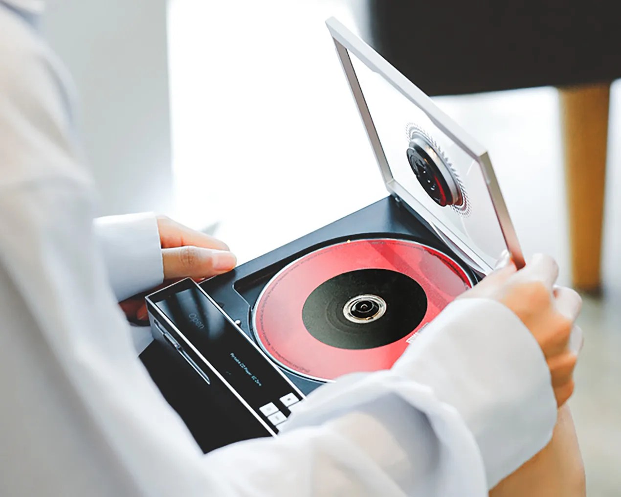 Person holding an open portable CD player with a red and black CD inside.