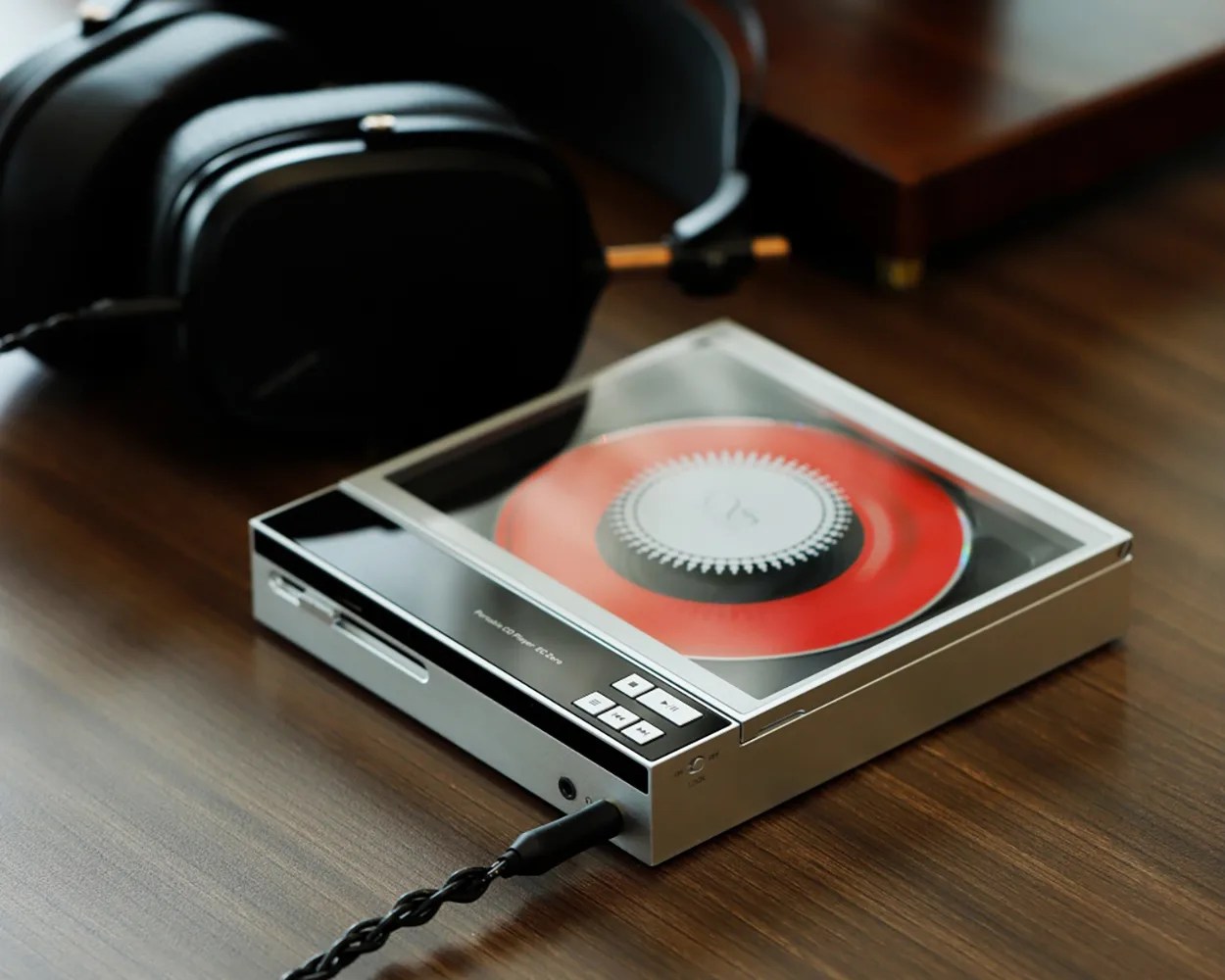 Silver portable record player with a red vinyl inside and black headphones on a wooden surface.