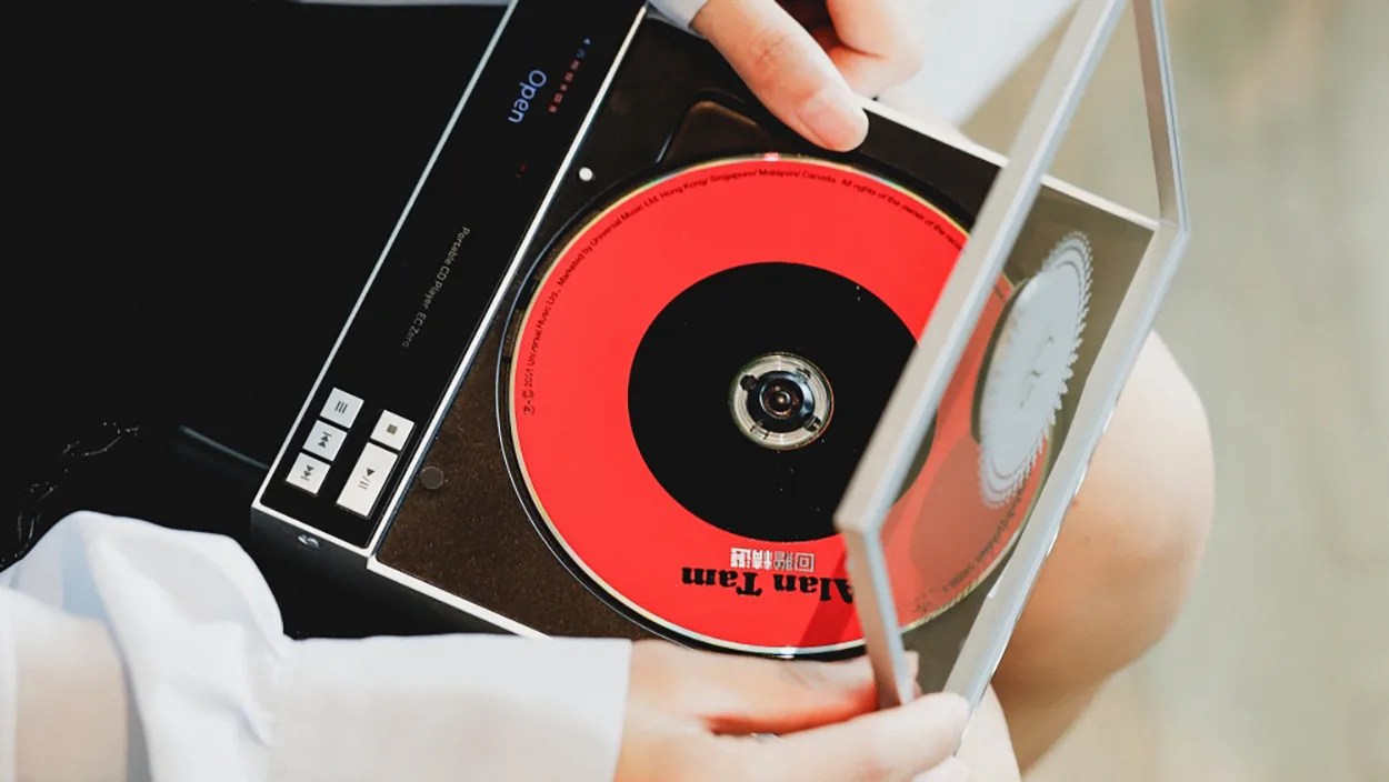 Person holding an open portable CD player with a red and black CD inside.