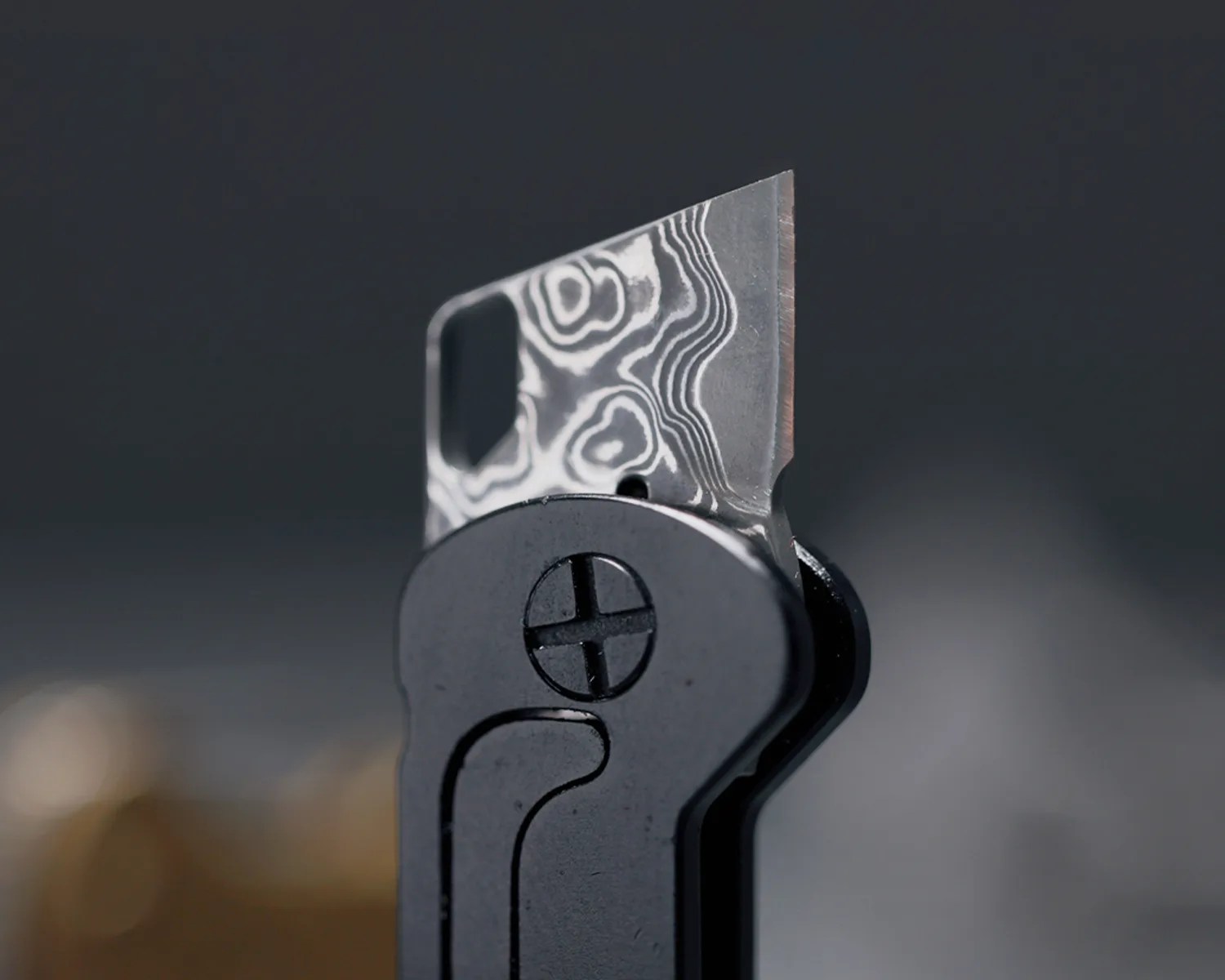 Close-up of a black folding knife with a patterned Damascus steel blade partially open.