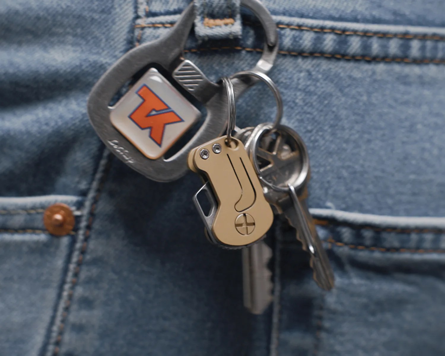 Set of metal keys and a gold-colored key organizer attached to a carabiner clipped to blue denim fabric.