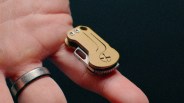 Compact gold and silver multi-tool with screws resting on a finger wearing a silver ring.
