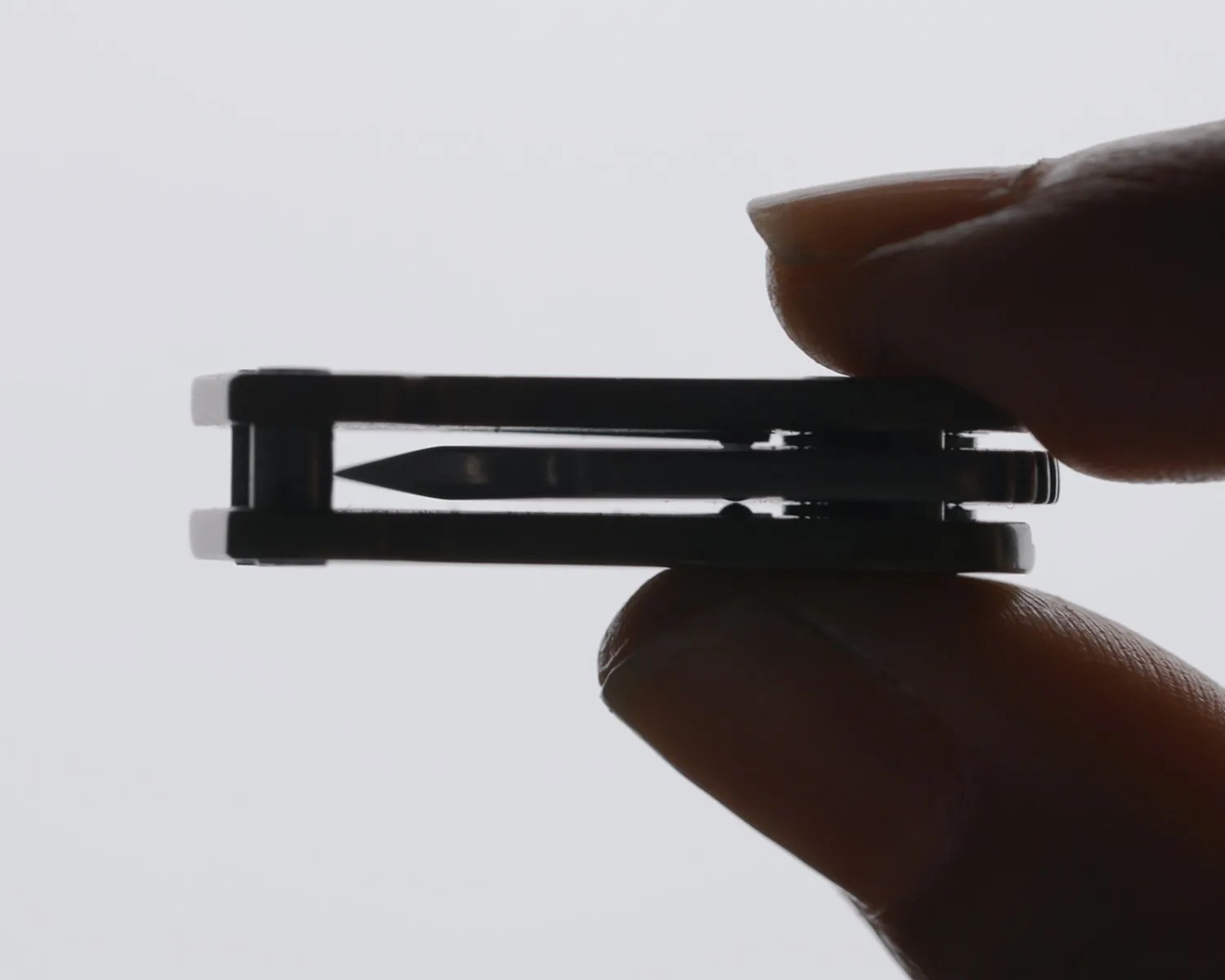 Black compact folding knife held between thumb and forefinger against a light background.