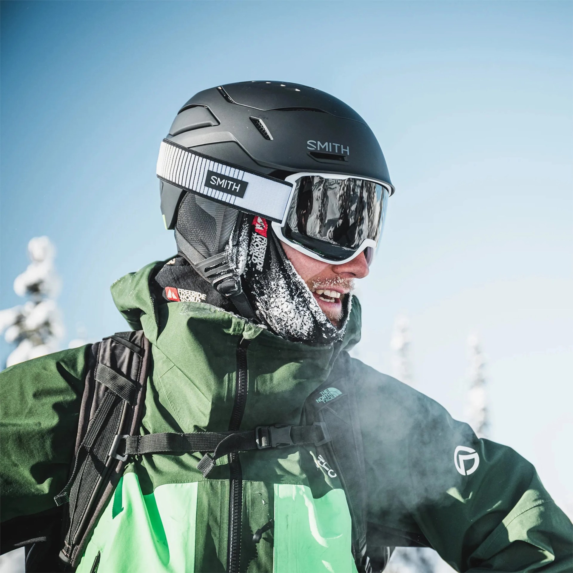 Person wearing a black Smith ski helmet and goggles with a green North Face jacket in a snowy outdoor setting.