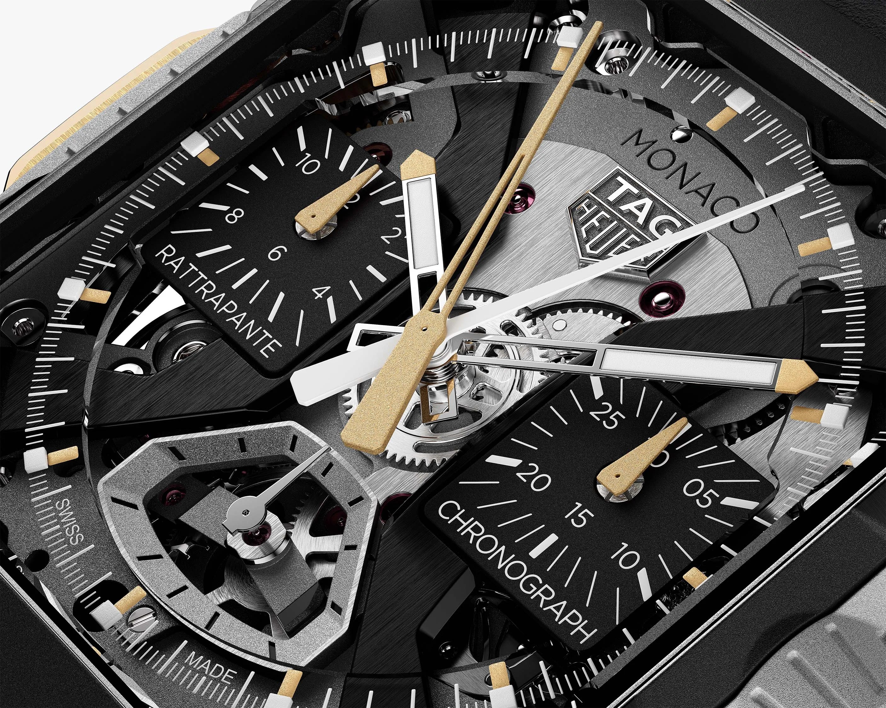 Close-up of a TAG Heuer Monaco watch face showing gold and white hands, black subdials labeled "Rattrapante" and "Chronograph," and visible mechanical gears.