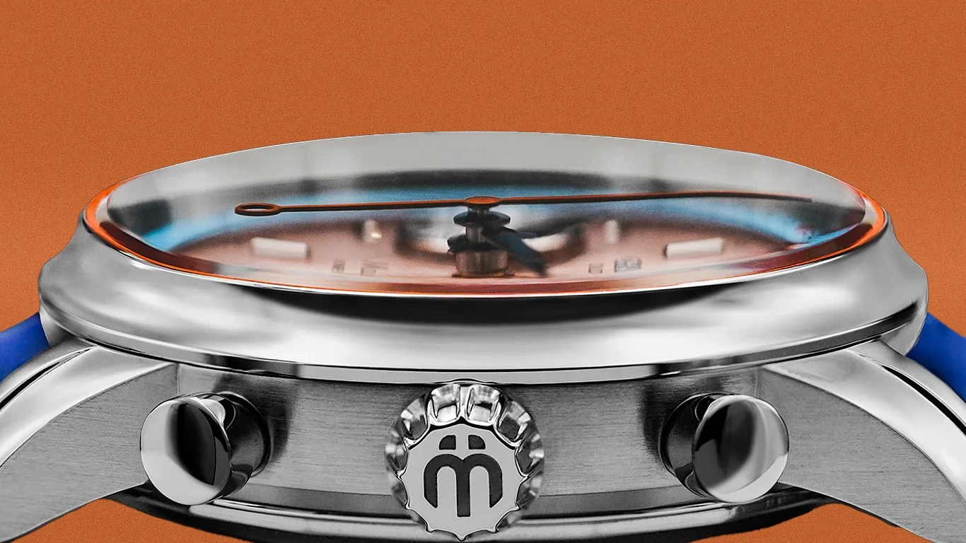 Close-up of a silver watch case with a crown featuring a stylized "m" logo and two push buttons, set against an orange background.