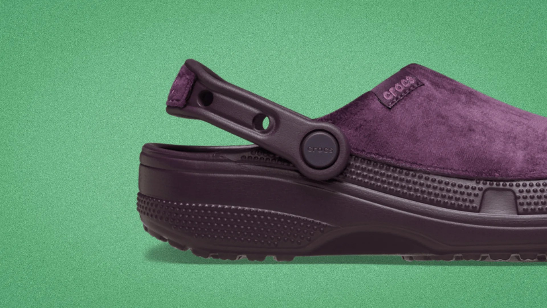 Purple suede Crocs clog with a textured sole and adjustable heel strap on a green background.