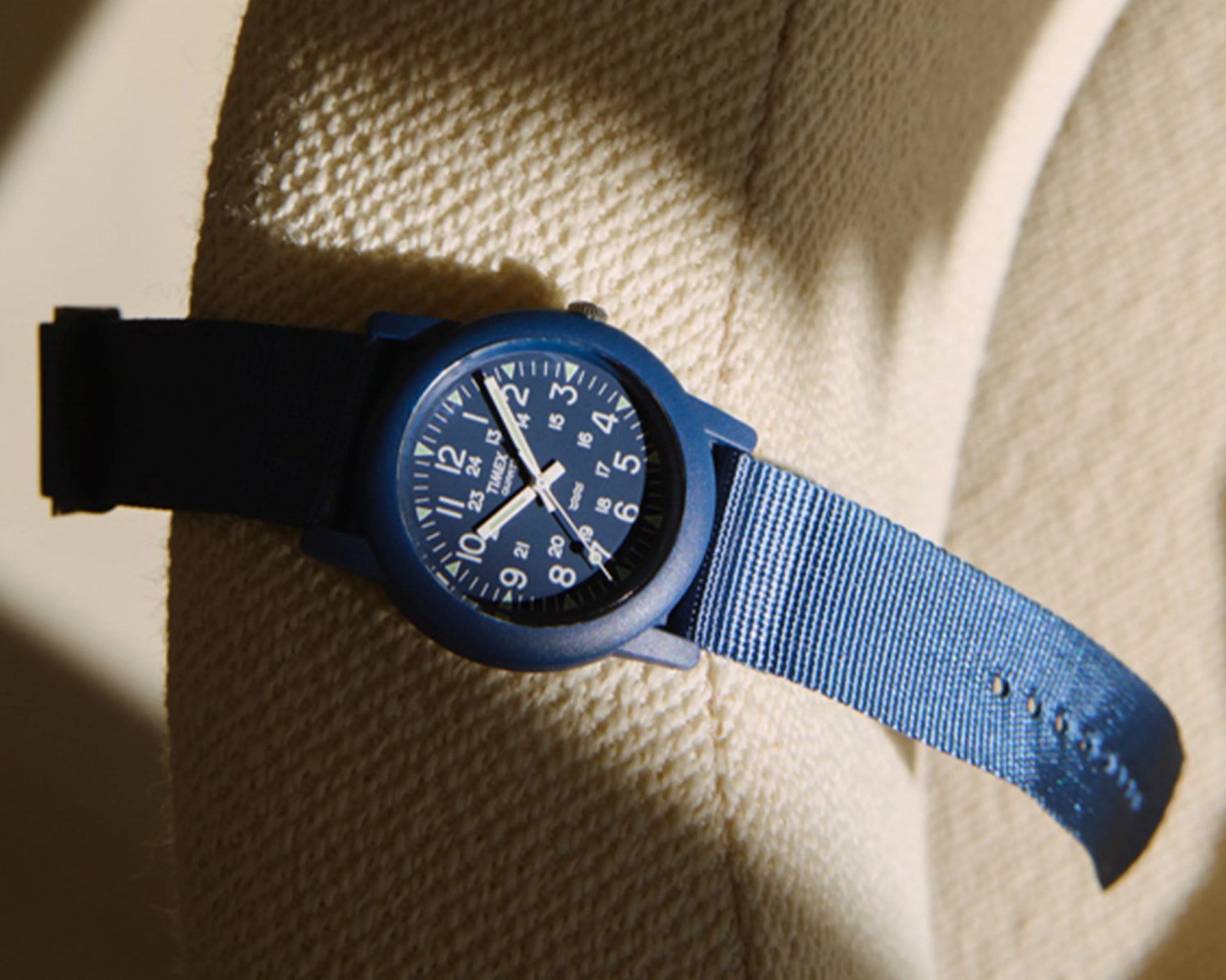 Blue Timex wristwatch with a fabric strap resting on a textured beige surface.