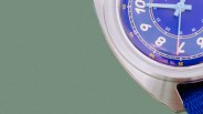 Close-up of a Timex watch with a blue dial, white numerals, yellow minute markers, and a blue woven strap.