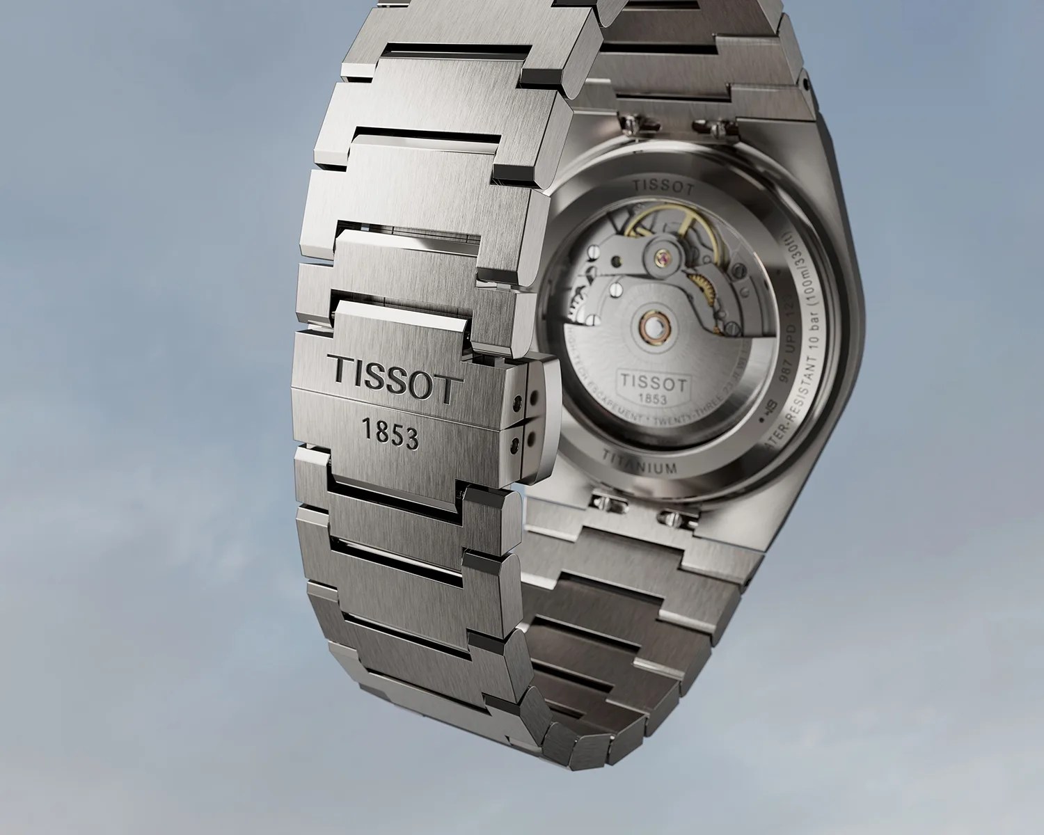 Brushed titanium Tissot watch bracelet and open case back showing mechanical movement.