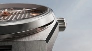 Close-up of a brushed titanium watch case with a polished bezel and a ridged crown on a light background.