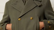 Olive green double-breasted coat with gold anchor-embossed buttons worn with hands in pockets.