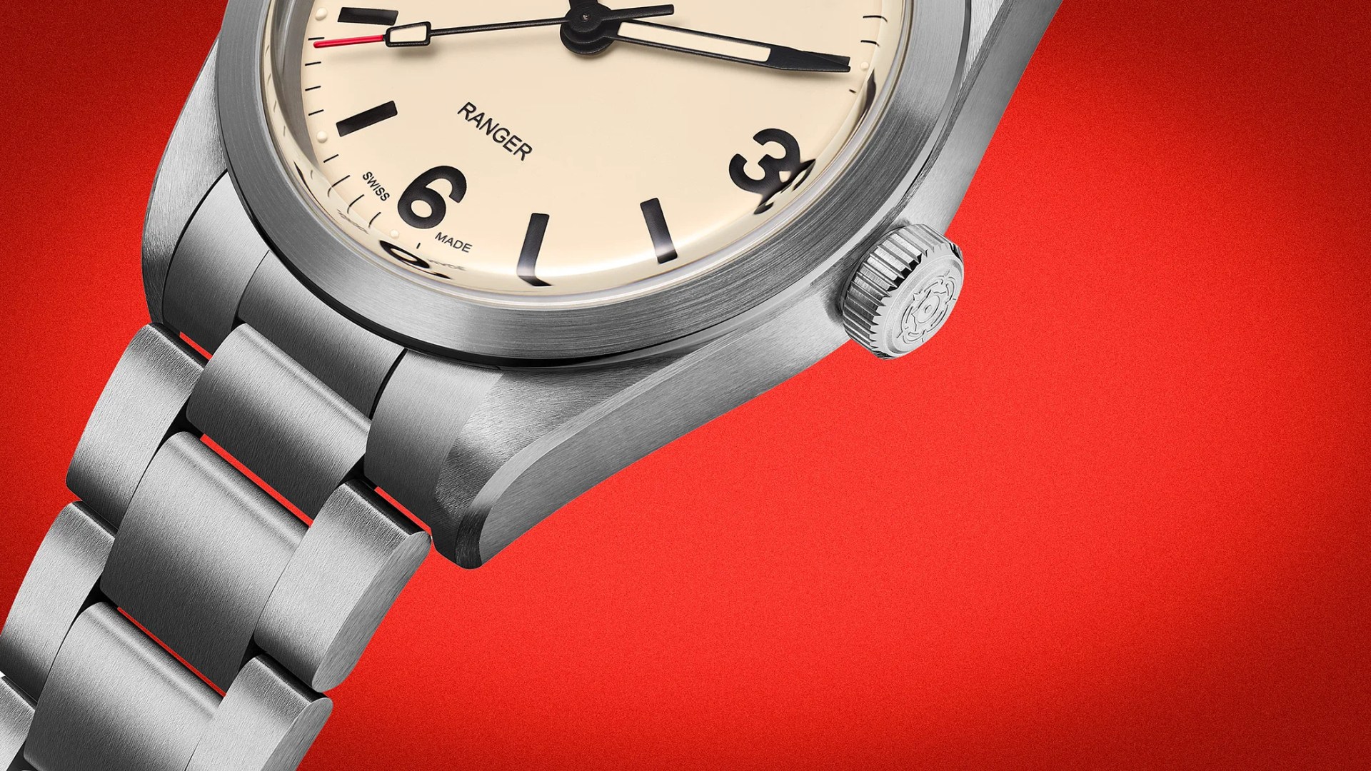 Close-up of a stainless steel wristwatch with a cream dial and black numerals on a red background.
