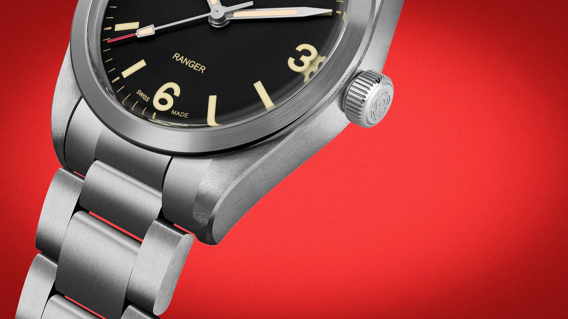 Close-up of a stainless steel wristwatch with a black dial, cream-colored numerals, and a brushed metal bracelet on a red background.