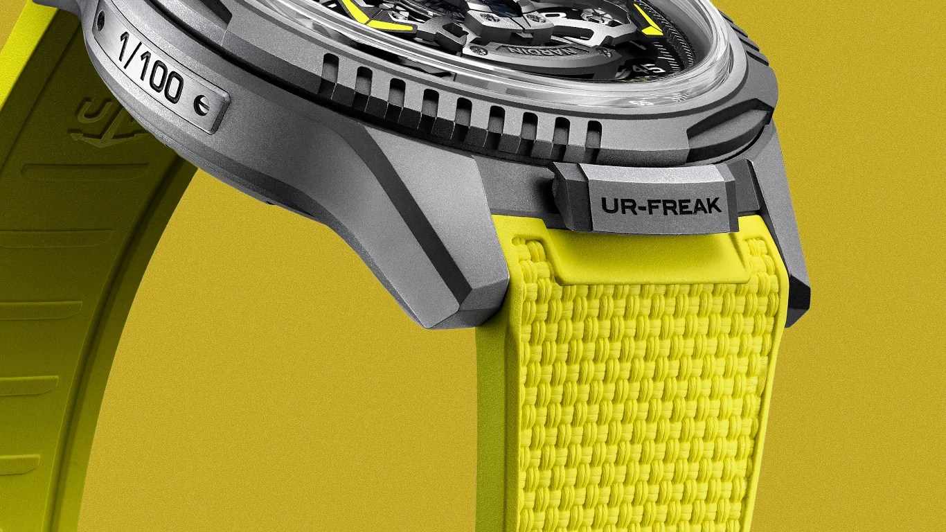 Close-up of a gray UR-FREAK watch case with a yellow rubber strap and a "1/100" limited edition metal plate.
