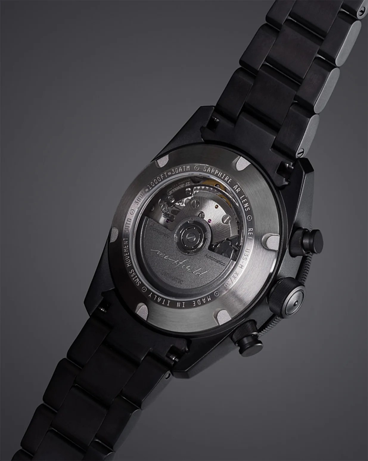 Back of a black metal wristwatch showing the automatic movement through a sapphire crystal case back.