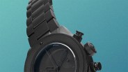 Black metal wristwatch with a textured bezel and three push buttons on a blue gradient background.
