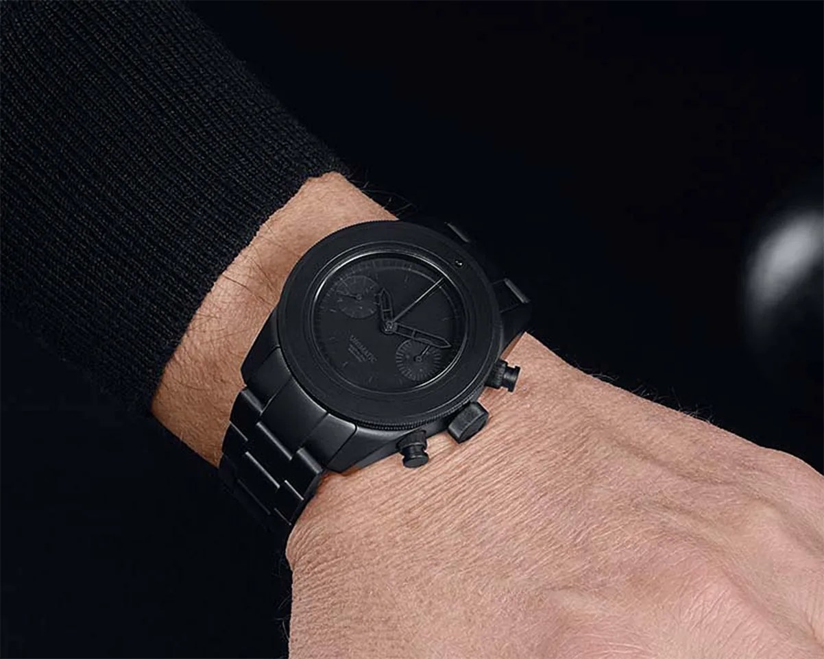 Matte black metal wristwatch with chronograph features worn on a wrist with a black sleeve.