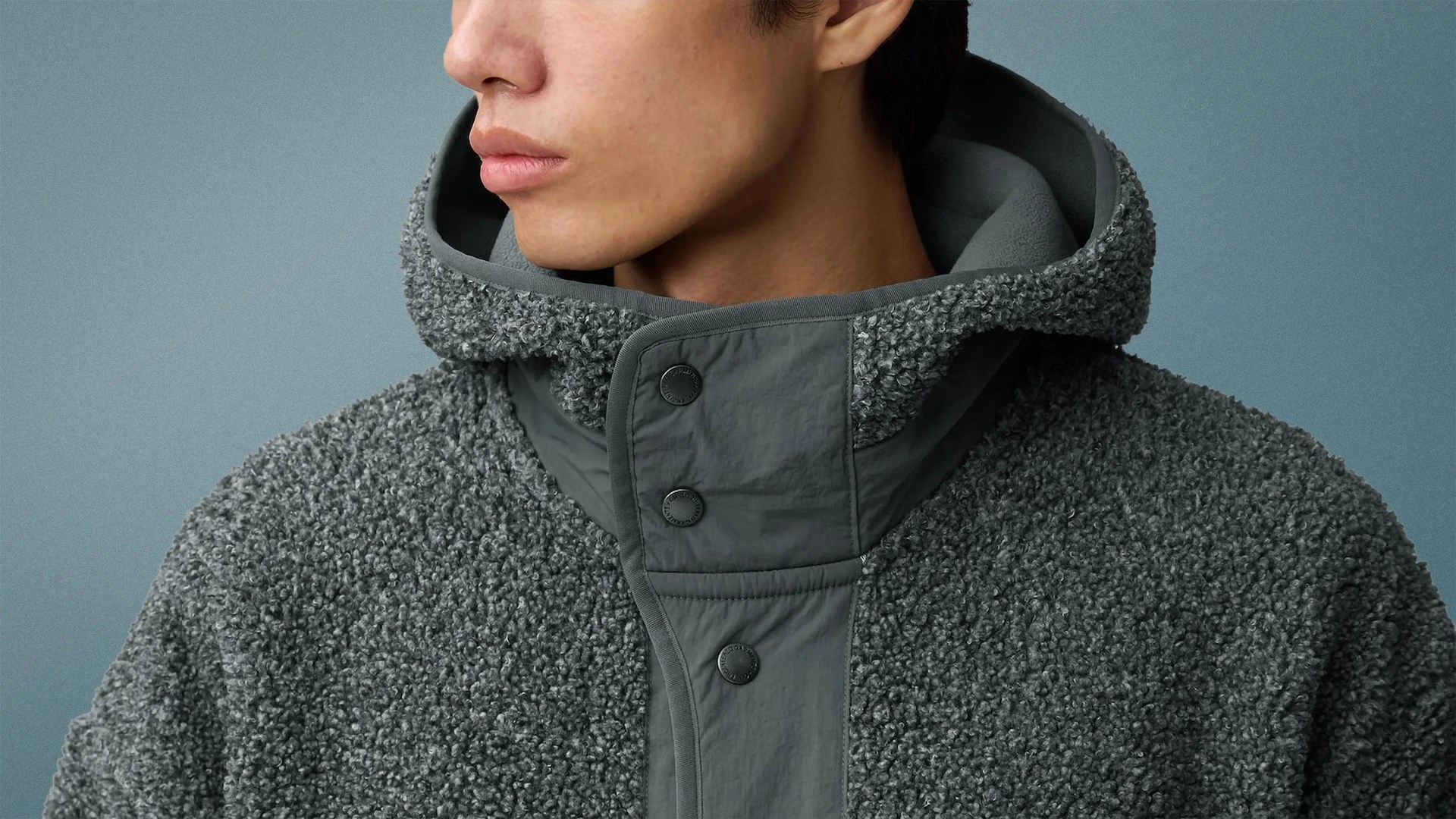 Close-up of a person wearing a textured dark gray fleece jacket with a hood and snap buttons.