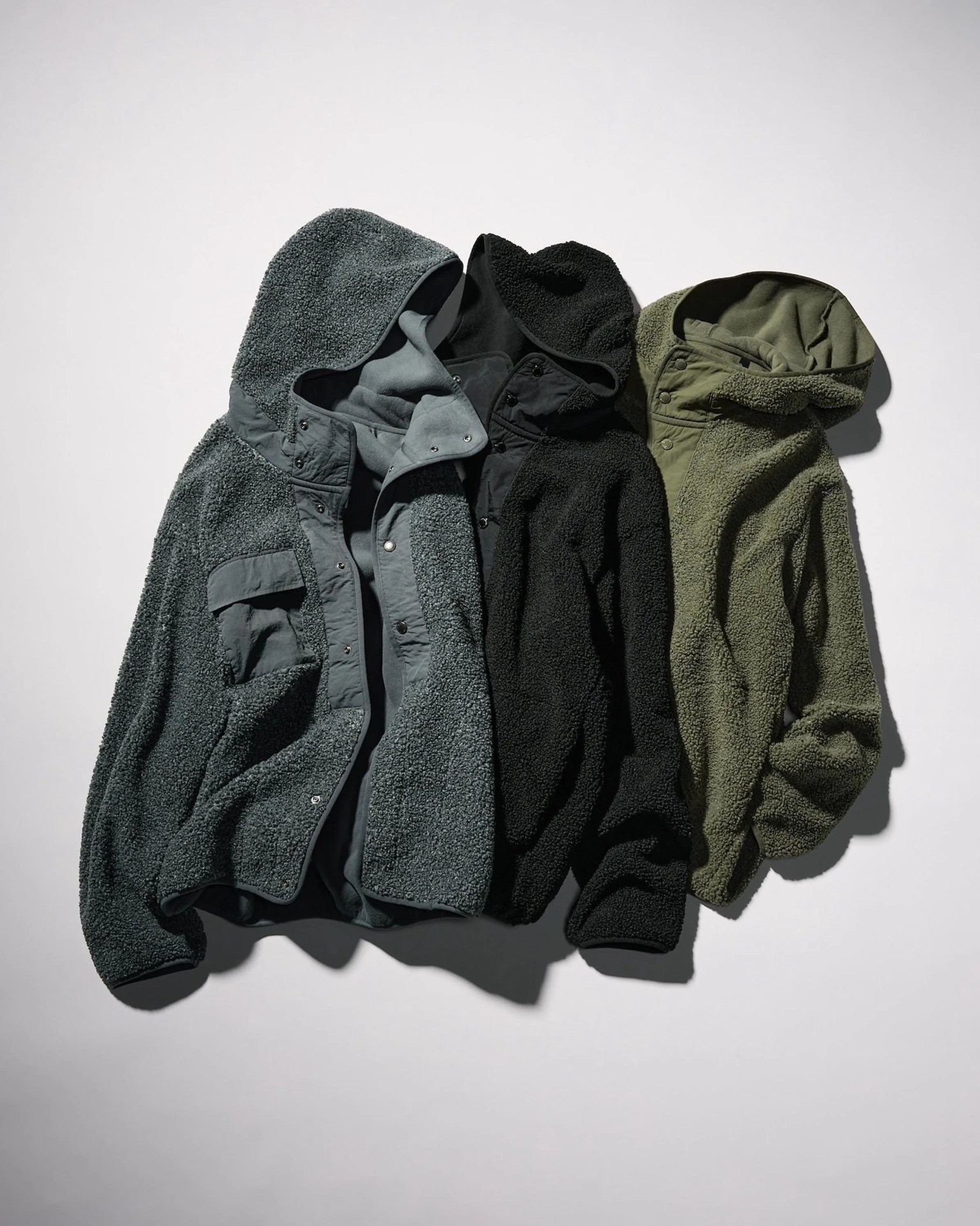 Three hooded fleece jackets in dark gray, black, and olive green laid flat on a white surface.