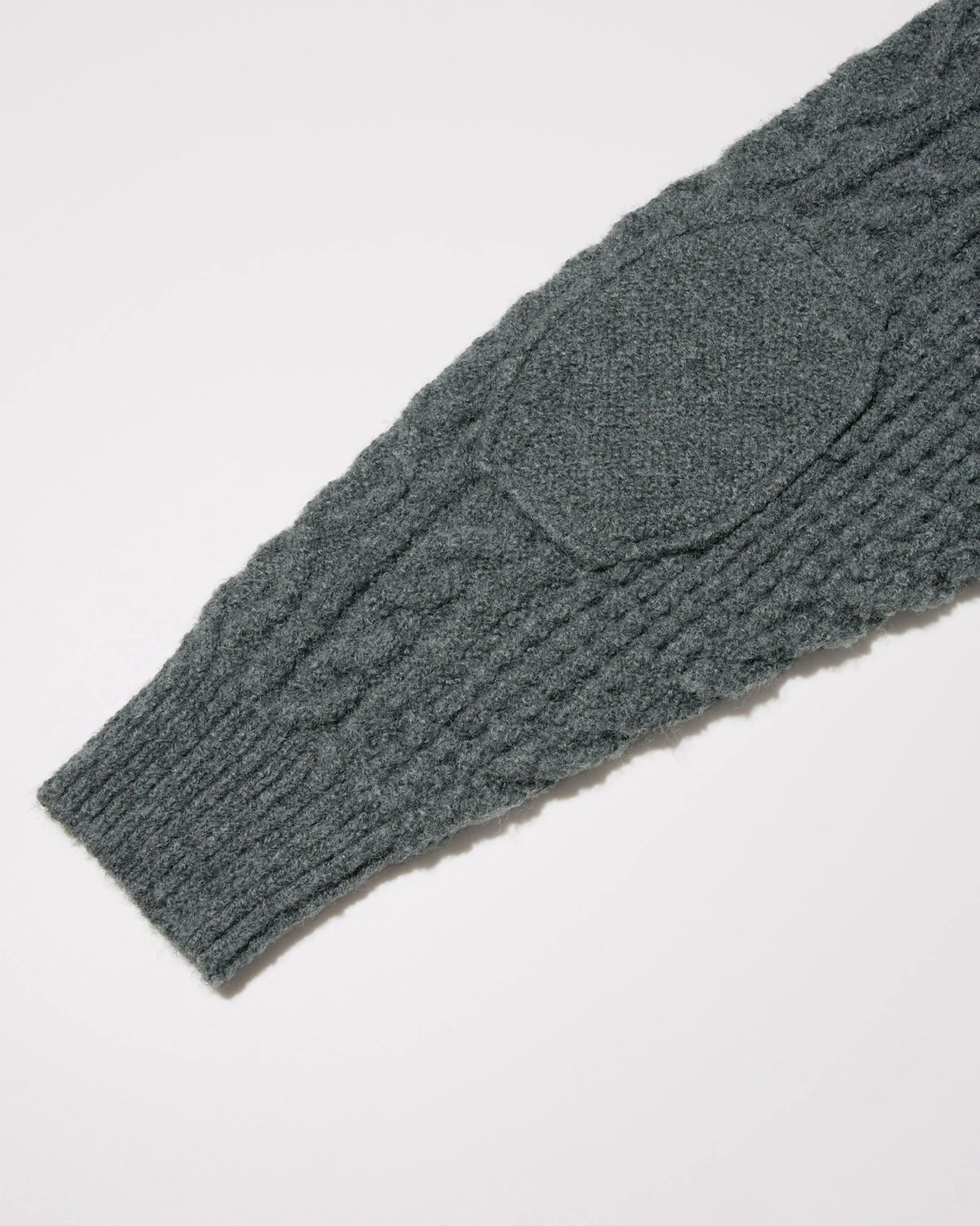 Dark gray knitted sweater sleeve with cable knit pattern and elbow patch on a white background.