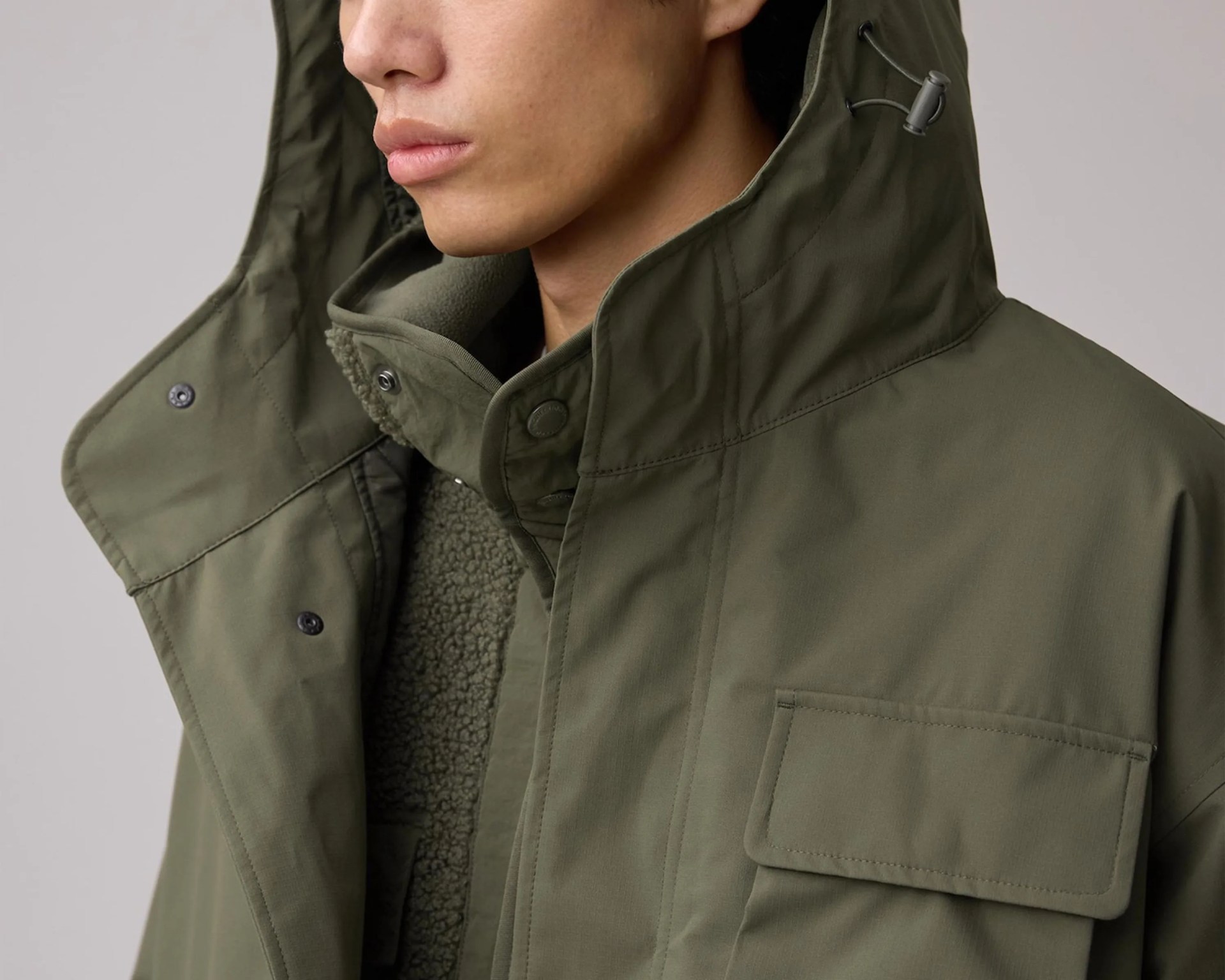 Close-up of a person wearing an olive-green jacket with a high collar and a textured inner lining.