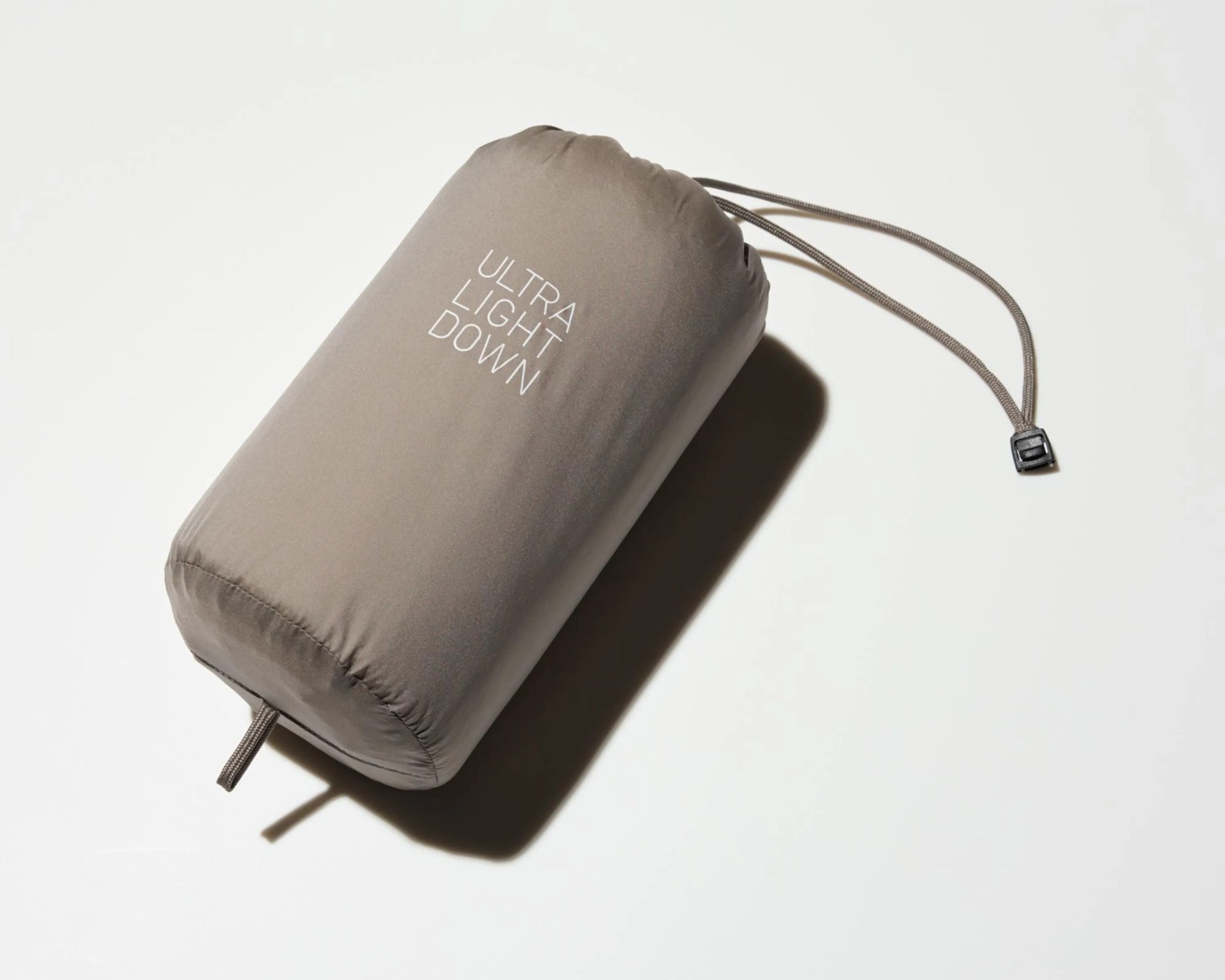 Gray cylindrical stuff sack with "ULTRA LIGHT DOWN" text and drawstring closure on a white surface.