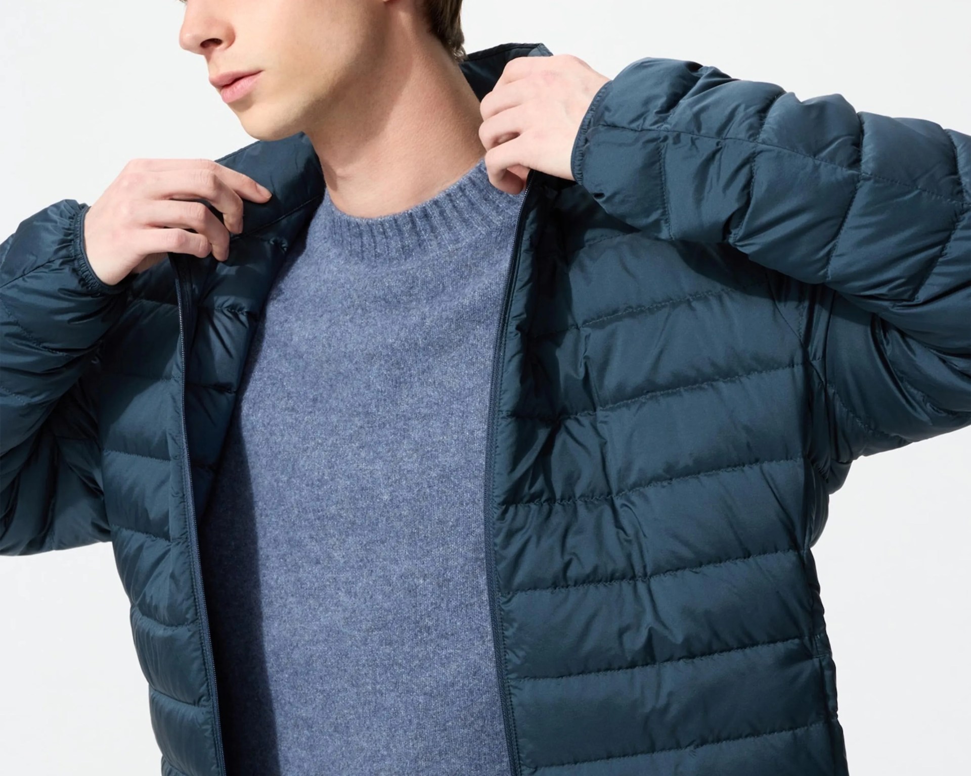 Man wearing a navy blue quilted puffer jacket over a light blue crewneck sweater.