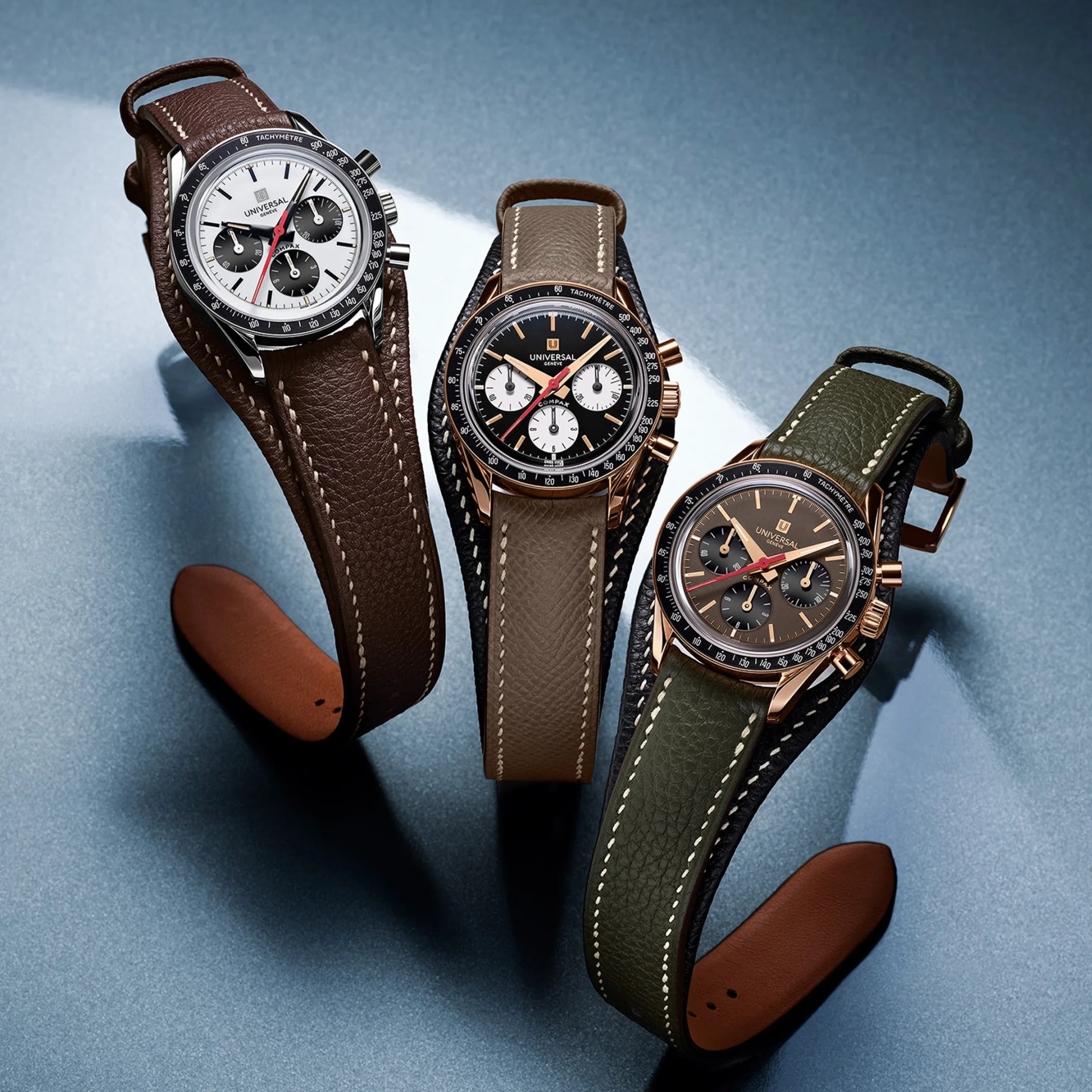 Three Universal Gen&egrave;ve wristwatches with leather straps in brown, taupe, and olive green on a blue surface.