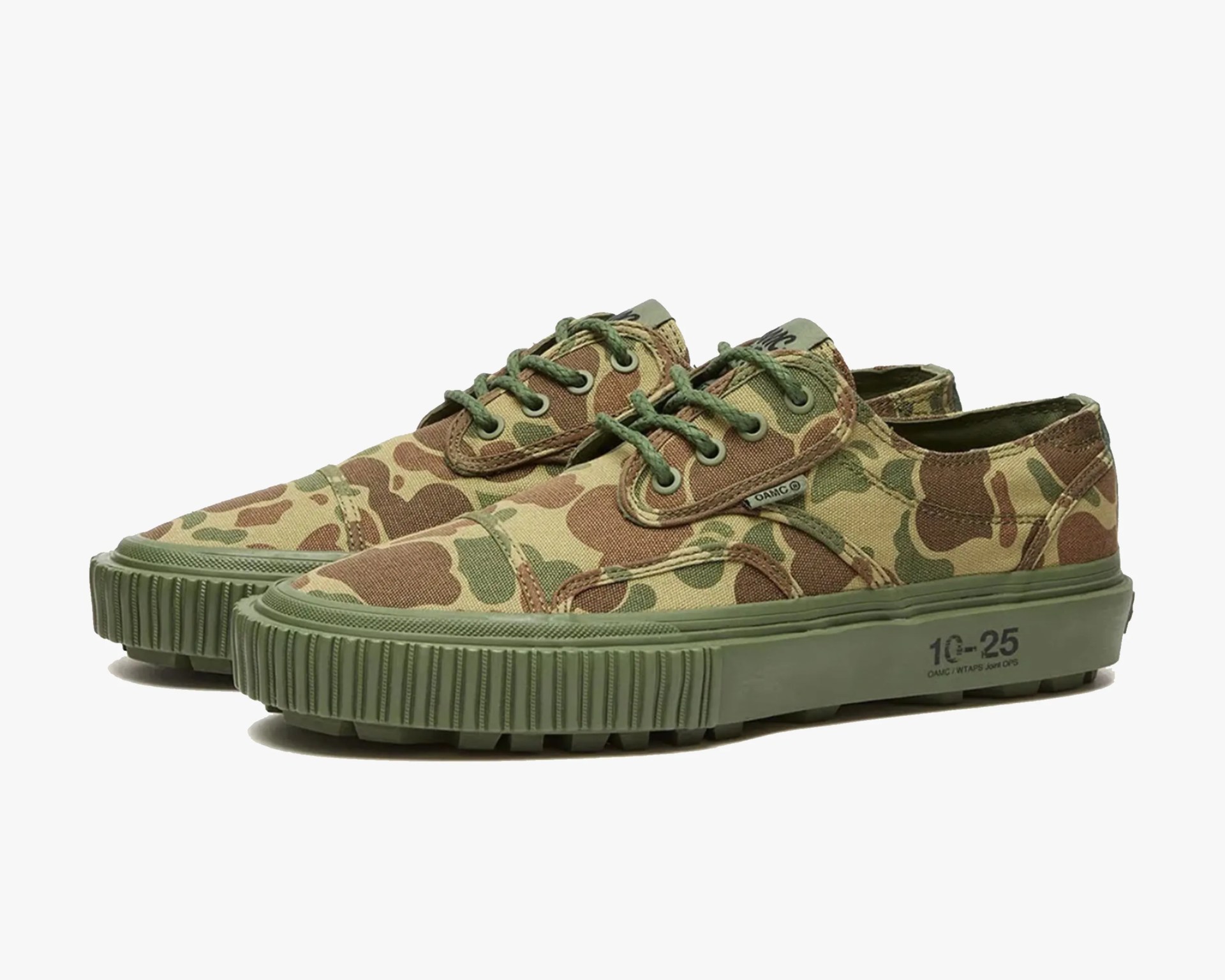 Pair of low-top sneakers with green and brown camouflage canvas uppers and thick green rubber soles.