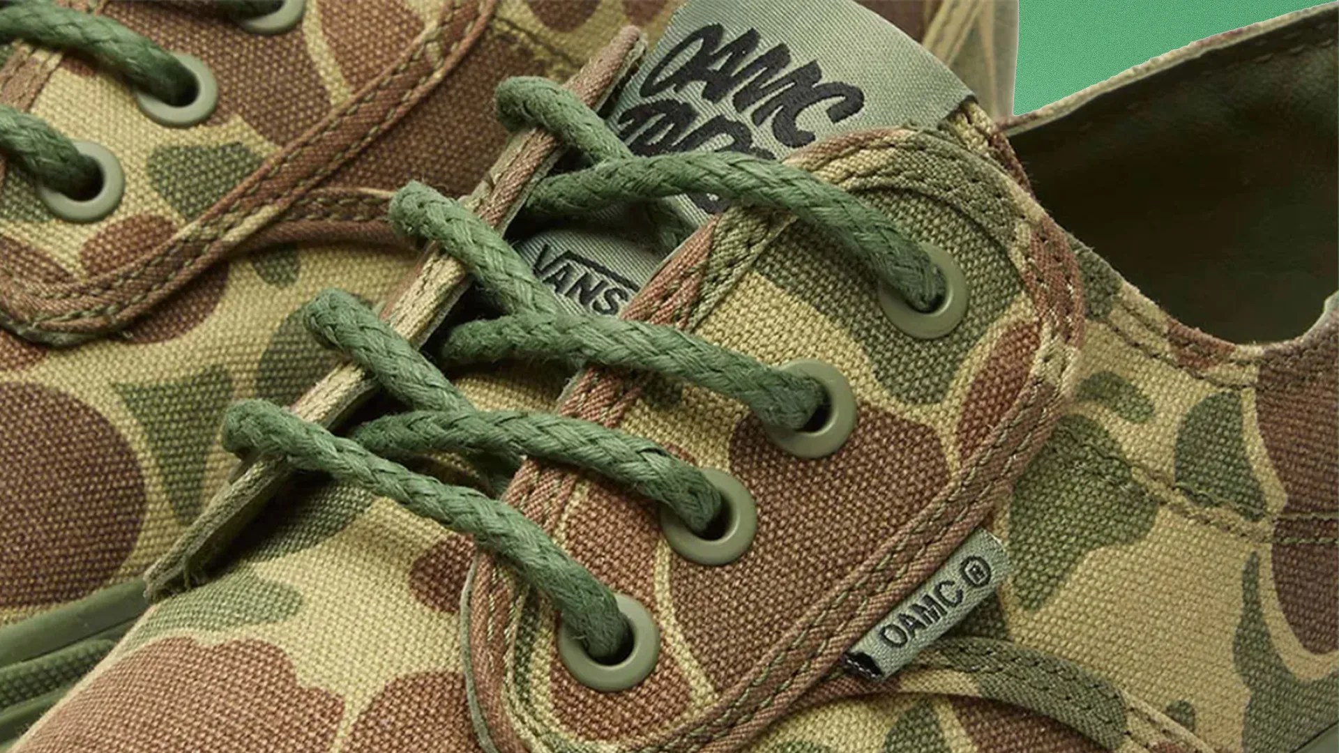 Close-up of camo-patterned Vans sneakers with green laces and OAMC branding on the tongue and side tag.