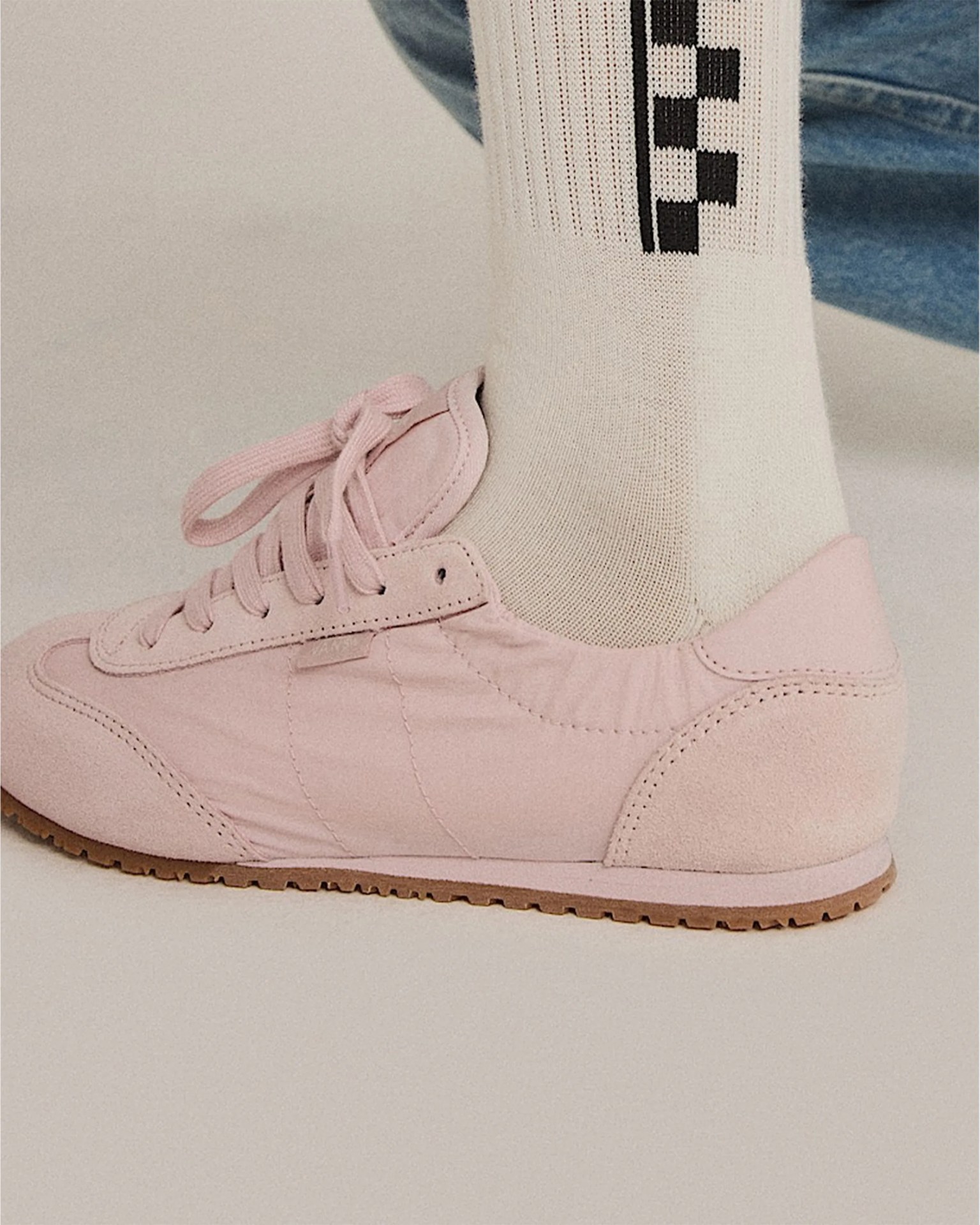 Light pink suede and fabric sneaker with laces worn with white socks featuring a black checkered pattern.