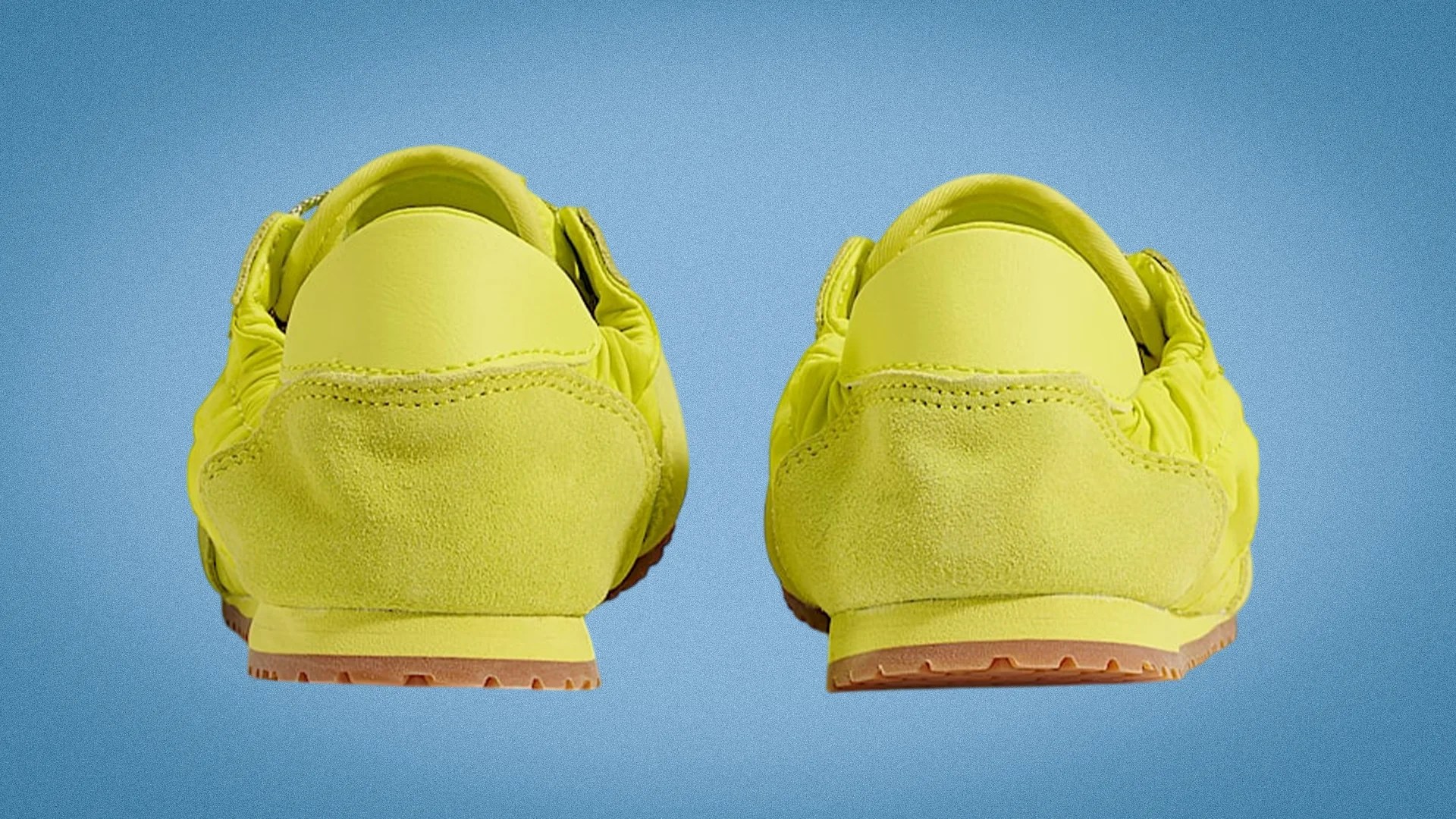 Pair of bright yellow suede sneakers with gum soles shown from the back against a blue background.