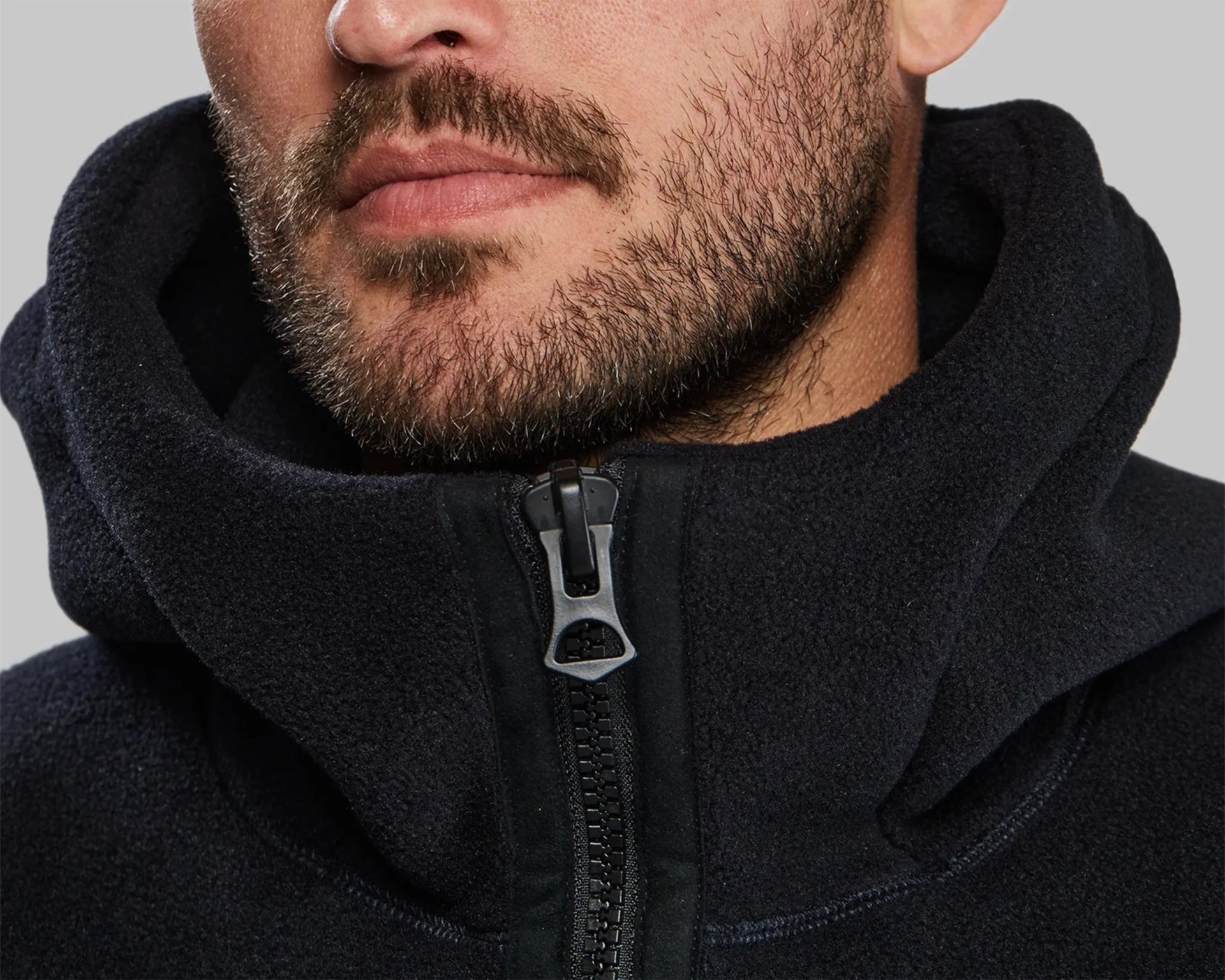 Close-up of a man's lower face with a short beard wearing a black fleece jacket zipped up to the neck.