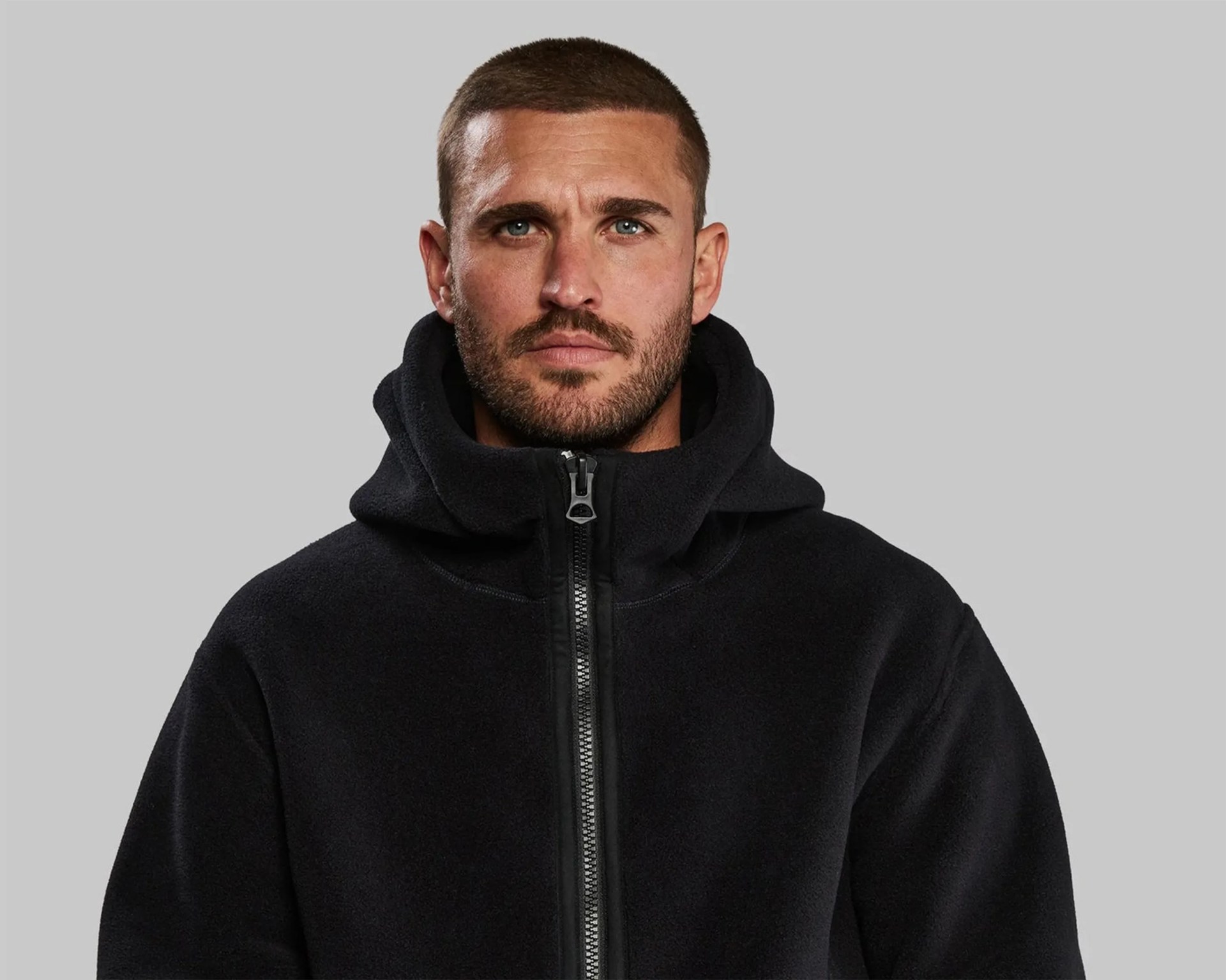 Man wearing a black fleece zip-up hoodie with a high collar against a gray background.