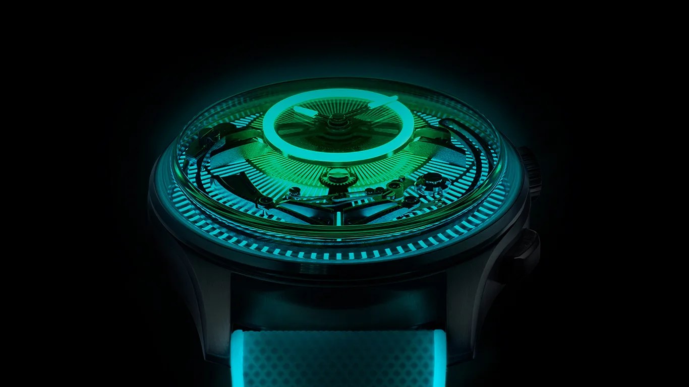 Close-up of a wristwatch with glowing green and blue luminescent dial and strap in a dark setting.