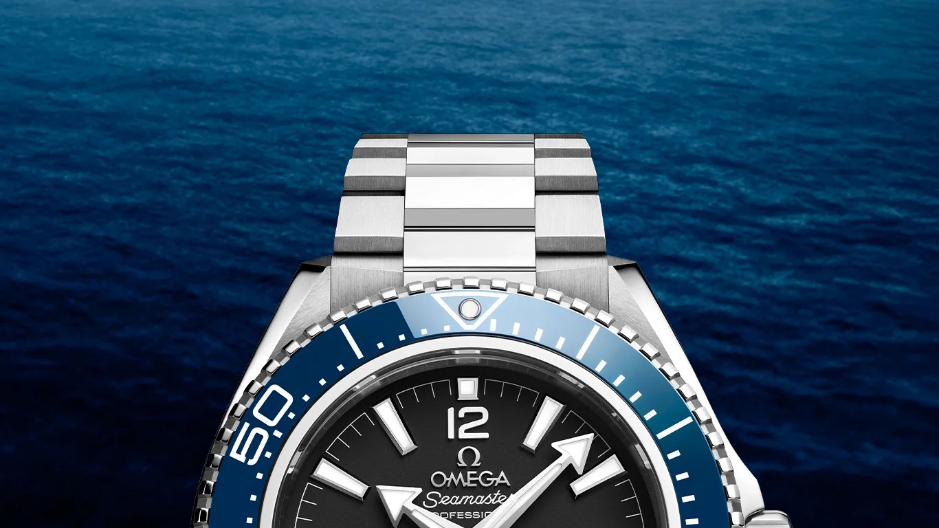 Silver Omega Seamaster wristwatch with blue bezel and black dial against a blue ocean background.