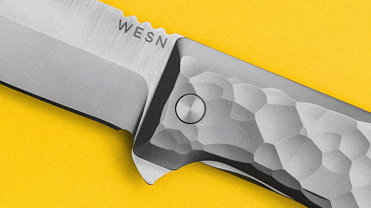Close-up of a silver WESN knife blade and textured handle on a yellow background.