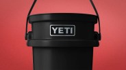 Black YETI bucket with a handle against a red background.