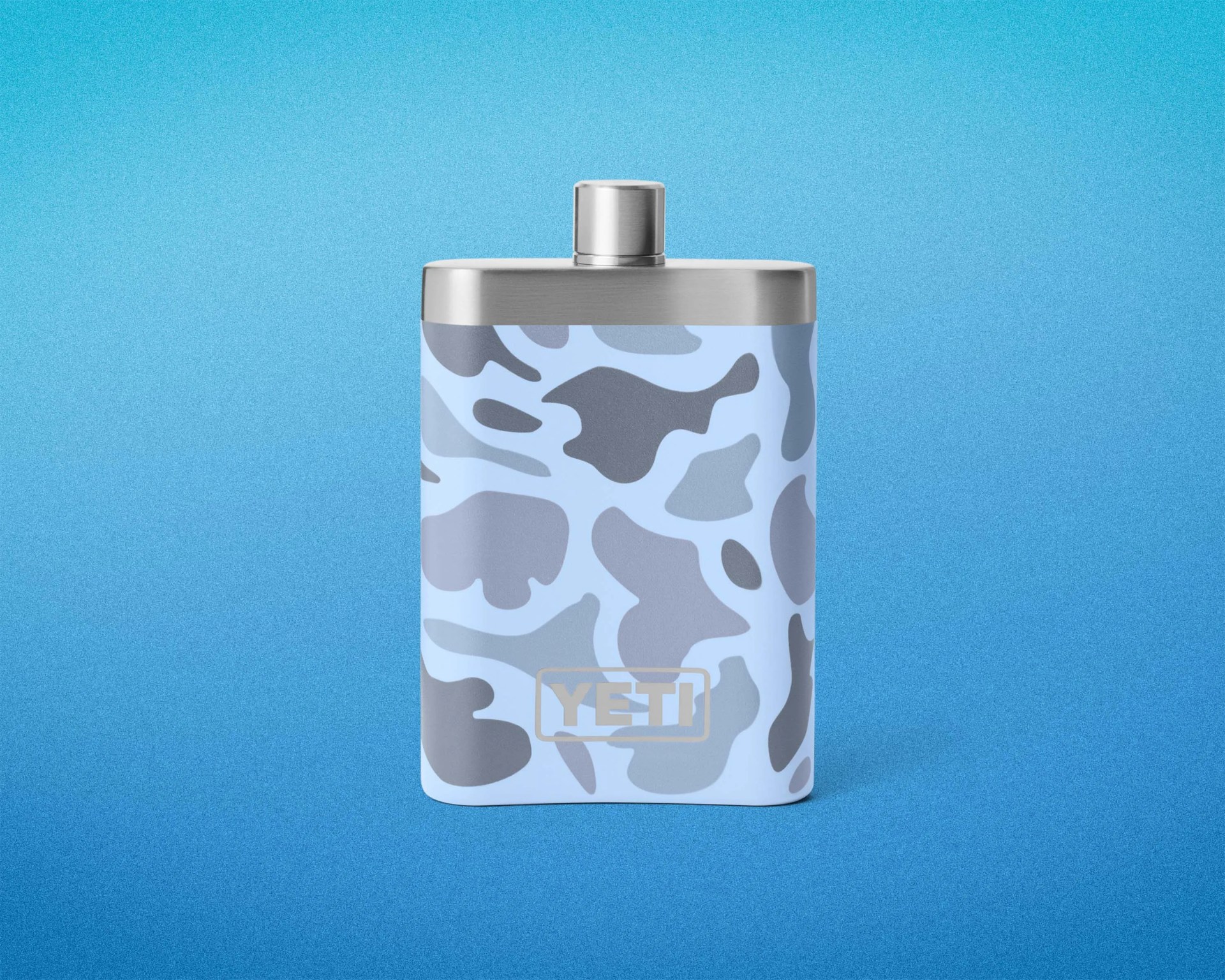 Blue and gray camo-patterned YETI stainless steel hip flask with screw cap on a blue gradient background.