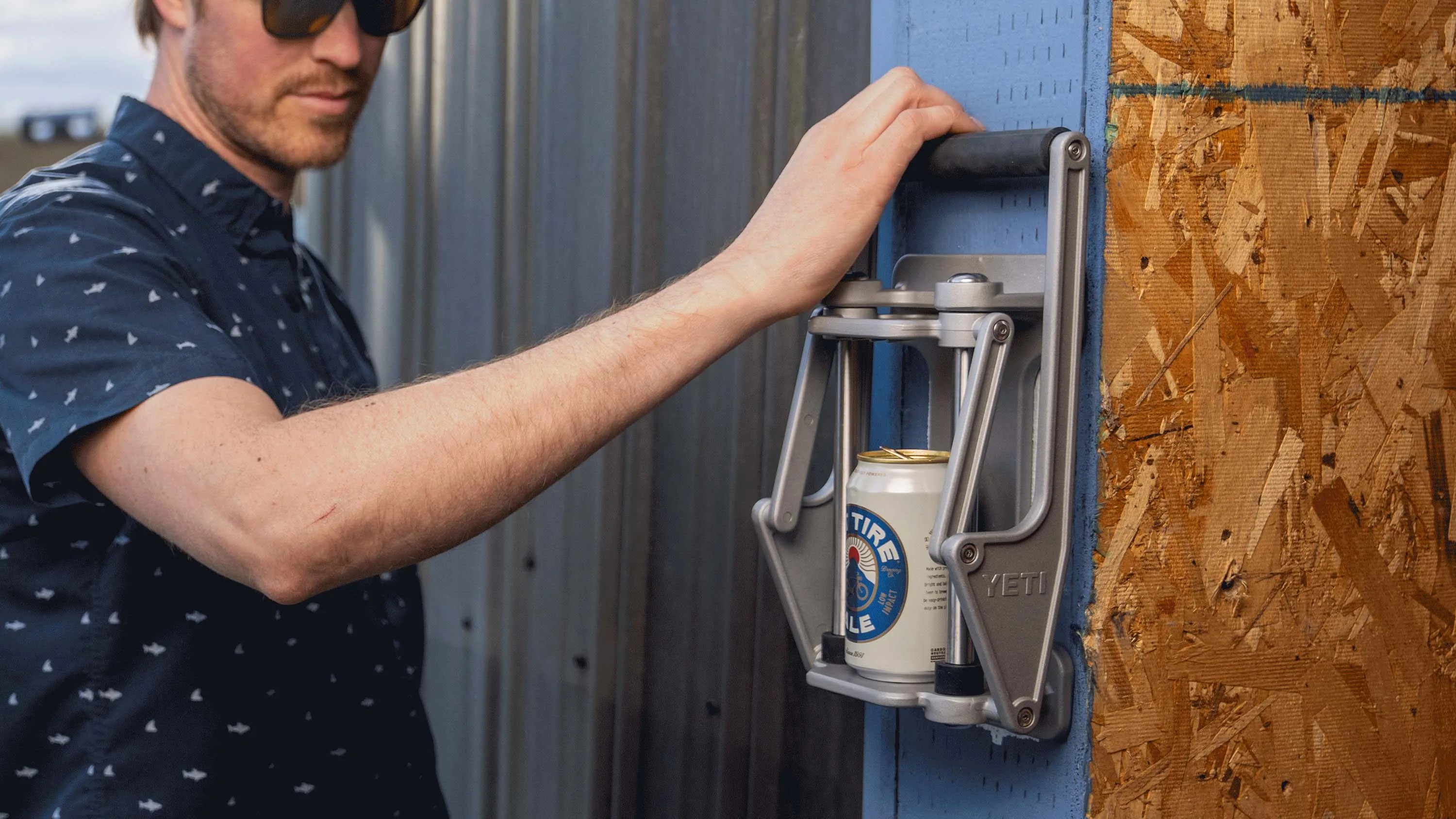 Man using a silver YETI can crusher mounted on a blue wooden surface with a can inside.