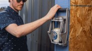 Man using a silver YETI can crusher mounted on a blue wooden surface with a can inside.